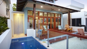 Een modern huis met een zwembad, een houten terras en een zitgedeelte buiten.