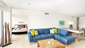 A modern living room with a blue sectional sofa, a wooden coffee table, and a dining area with a white table and chairs.