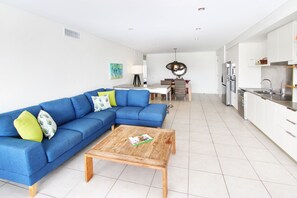 A modern living room with a blue sectional sofa, a wooden coffee table, and a dining area with a table and chairs.