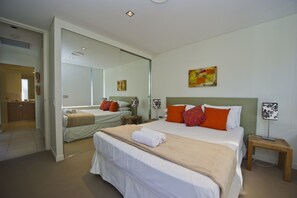 A modern hotel room with a large bed, a mirror, two bedside tables with lamps, and artwork on the wall.