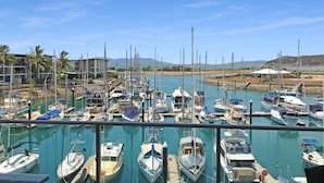 A marina with various boats docked, a clear sky, and a view of the surrounding landscape.