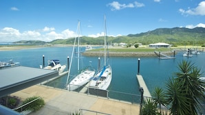 A marina with boats docked, a dock, and a building in the background. - Blue on Blue Superior Studio Room 1241 (Nelly Bay)