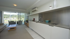 A modern kitchen with a large island, a built-in sink, and a view of the marina through large windows. - Blue on Blue Superior Studio Room 1241 (Nelly Bay)