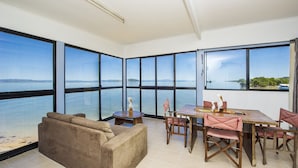 Um quarto espaçoso com uma grande janela com vista para um corpo de água, uma área de jantar com mesa e cadeiras de madeira, e um sofá bege.