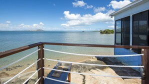 Visão clara de uma área costeira com um deck de madeira e guarda-corpo de metal, com vista para o mar.