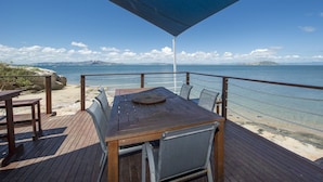 Um deck de madeira com mesa e cadeiras com vista para a praia e o mar.