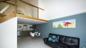 Una sala de estar moderna con un sofá de cuero negro, un comedor con sillas blancas y una cocina al fondo.