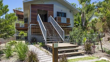 A modern two-story house with a wooden deck and a staircase leading to the entrance.