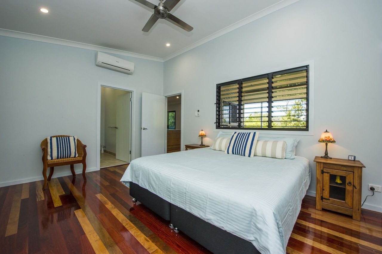 A bedroom with a bed, a chair, a nightstand, a window with blinds, and an air conditioning unit.