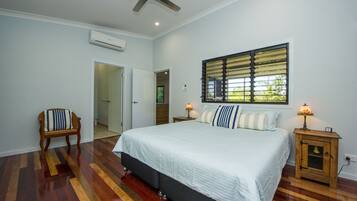 A bedroom with a bed, a chair, a nightstand, a window with blinds, and an air conditioning unit.