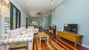 A living room with striped sofas, a wooden coffee table, a TV on a wooden stand, and a ceiling fan.
