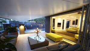 Un espacio de sala abierto con un conjunto de sofás, una mesa de centro y un otoman amarillo. Hay una puerta de vidrio que da a una zona de cocina.
