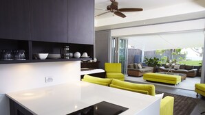 Una cocina moderna con encimera blanca y placa de inducción negra, un sofá amarillo, y un comedor con mesa y sillas.