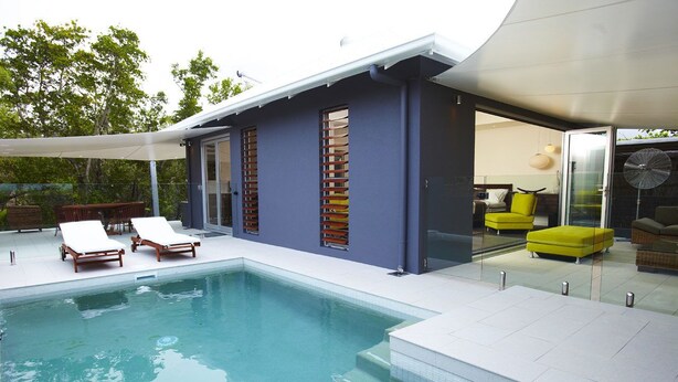Una casa moderna con piscina, mobiliario exterior y puerta de cristal que da a un espacio interior.