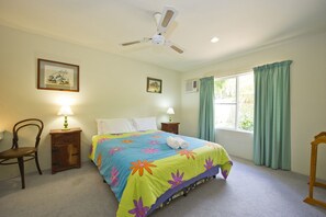 A bedroom with a bed, two bedside lamps, a ceiling fan, a window with curtains, and a chair.