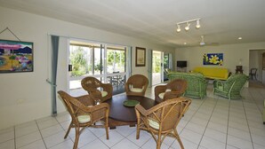 A spacious living room with a dining area, large windows, and green wicker furniture. - John's Tropical Island Home (Nelly Bay)