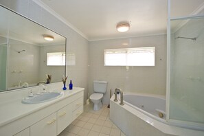 A modern bathroom with a large mirror, a sink, a toilet, and a bathtub.