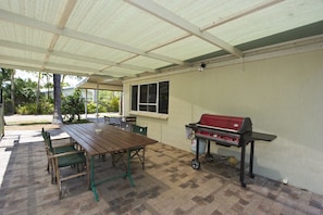 An outdoor patio with a wooden table and chairs, a barbecue grill, and a covered area with a window.