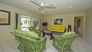 A living room with wicker furniture, a yellow sofa, a ceiling fan, and a painting on the wall. - John's Tropical Island Home (Nelly Bay)