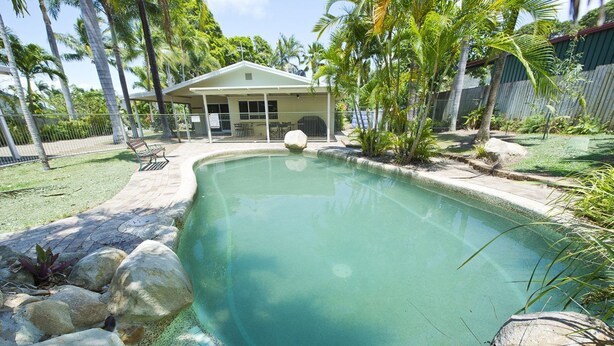 A swimming pool with a covered seating area, surrounded by rocks and palm trees. - John's Tropical Island Home (Nelly Bay)