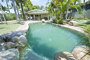 A swimming pool with a covered seating area, surrounded by rocks and palm trees. - John's Tropical Island Home (Nelly Bay)