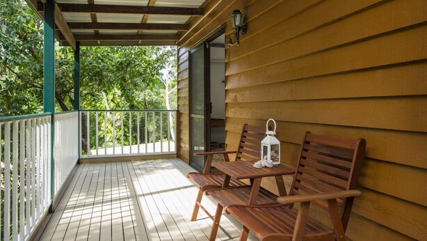 Una terraza de madera con techo, dos sillas de madera, una mesita y un farol.