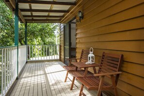A wooden deck with a covered area, two wooden chairs, a small table, and a lantern. - Koorakai (Arcadia)