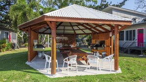 A covered outdoor seating area with a grill, white plastic chairs, and a concrete floor. - Kooyong Apartment 3 (Arcadia)