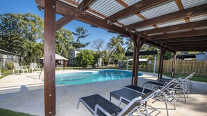 A covered outdoor swimming pool area with lounge chairs and a pergola structure. - Kooyong Apartment 3 (Arcadia)