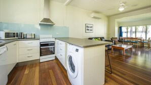 Een kleine keuken met een ingebouwde oven, magnetron en wasmachine, een eethoek met een tafel en stoelen, en een zithoek met een bank en salontafel.