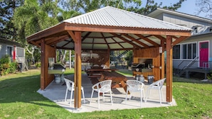 Un espace extérieur abrité, aménagé avec un barbecue, des chaises en plastique blanc et un sol en béton.