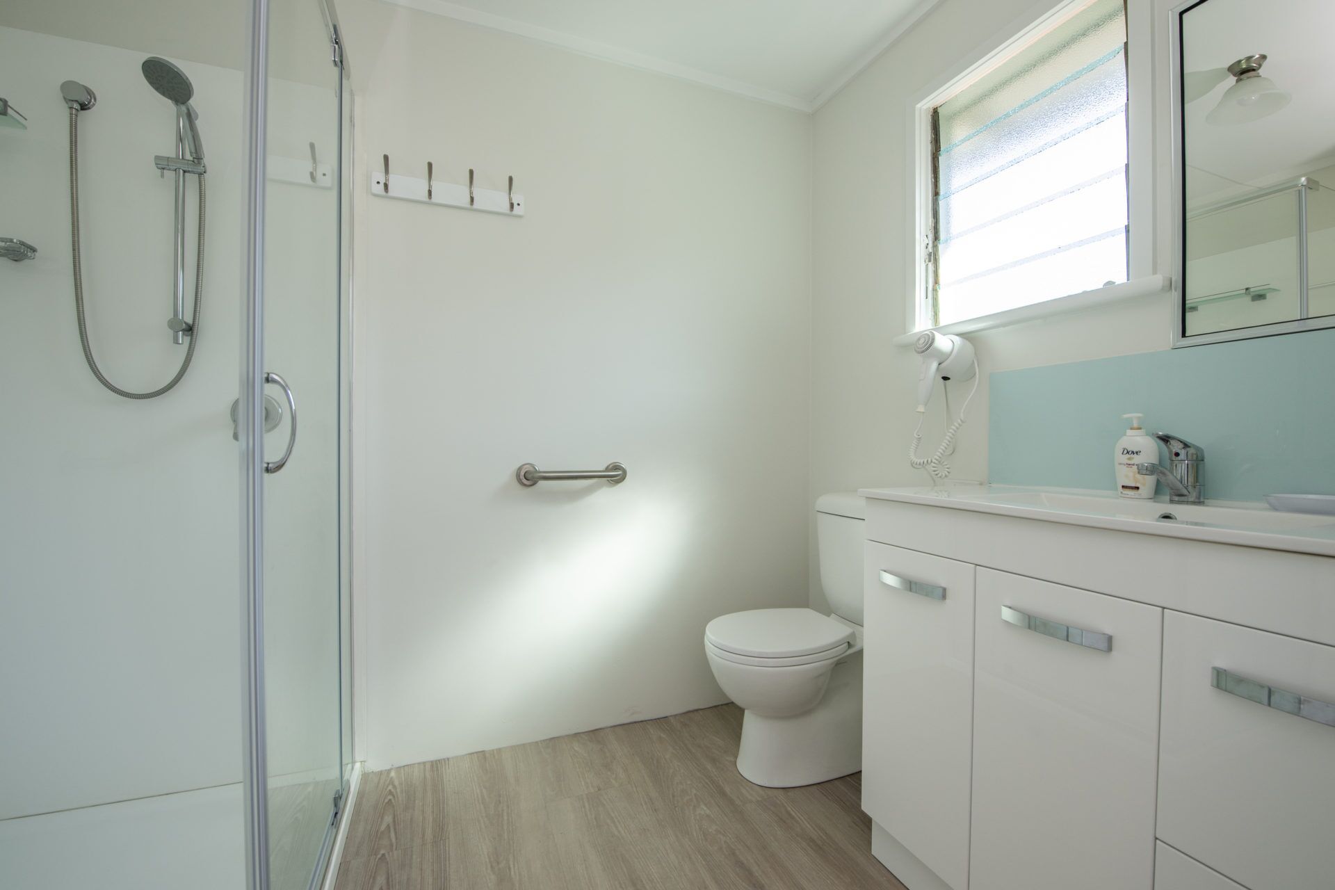 A modern bathroom with a glass shower enclosure, a white toilet, and a vanity with a mirror and a hairdryer.