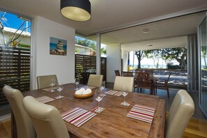 A dining area with a wooden table, beige chairs, and a view of the outdoors. - Maggies Beachfront Apt. 1 (Horseshoe Bay)