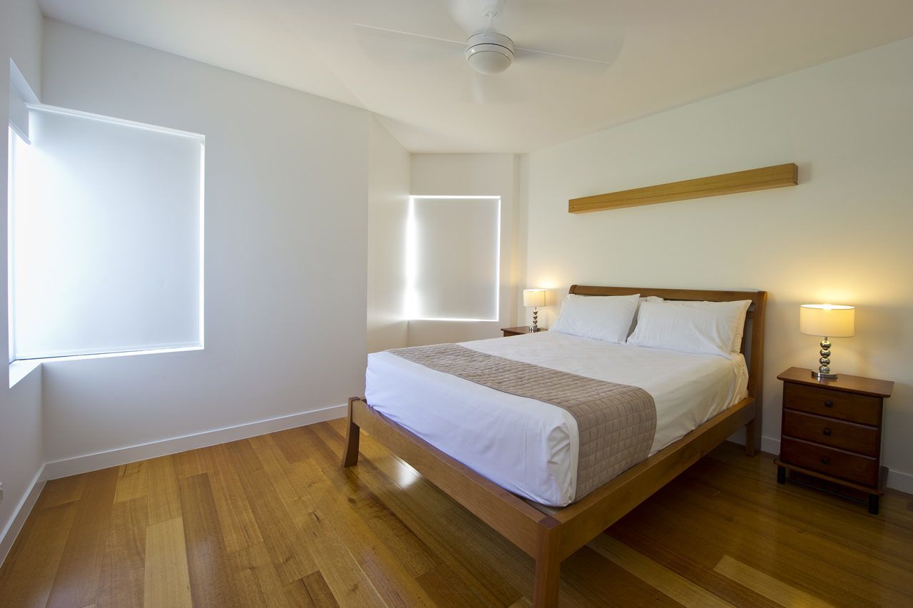 A bedroom with a wooden bed, bedside lamps, a ceiling fan, and a window with blinds.