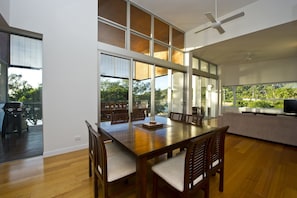 Enjoy meals in this dining area with a large table and chairs, surrounded by windows offering a view of the lush landscape.