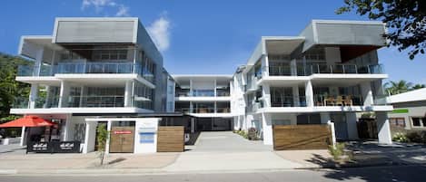A modern multi-story building with balconies, a covered entrance, and a clear sky.