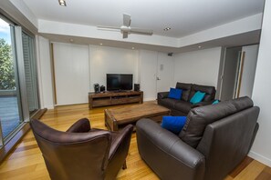 Un salon moderne avec un canapé, des fauteuils en cuir, une table basse et un téléviseur.