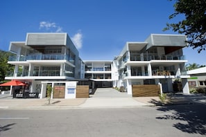 A modern multi-story building with balconies, a covered entrance, and a clear sky.