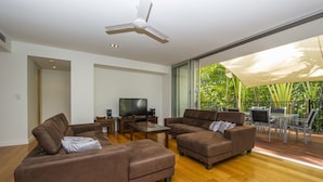 Uma sala de estar moderna com televisão de tela plana, dois sofás marrons, uma mesa de centro e um ventilador de teto.