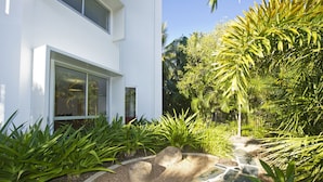 Um edifício moderno e branco, com amplas janelas e um jardim bem cuidado, com plantas tropicais e um caminho de pedra.