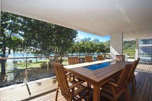 A wooden deck with a glass balustrade overlooking a lush green landscape and a body of water. - Maggies Beachfront Apt. 3 (Horseshoe Bay)