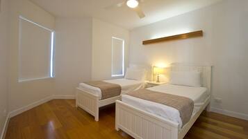 A bedroom with two single beds, a ceiling fan, and a window with blinds.