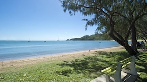 A beach with a bench and a tree, boats in the water, and a distant shoreline. - Maggies Beachfront Apt. 7 (Horseshoe Bay)