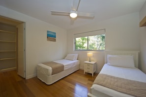 A bedroom with two single beds, a ceiling fan, a window with a view of trees, and a door to a closet.