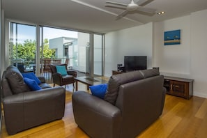 A modern living room with leather sofas, a flat-screen TV, and a balcony with a dining area. - Maggies Beachfront Apt. 8 (Horseshoe Bay)
