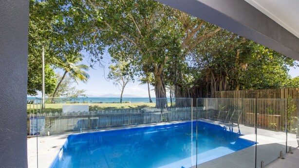 Una piscina con barrera de vidrio, rodeada de árboles y vistas al océano.