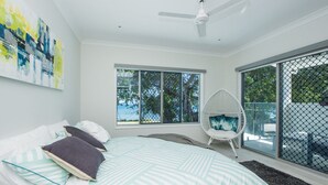 Un dormitorio moderno con cama, ventilador de techo blanco, ventana grande y vista al exterior.