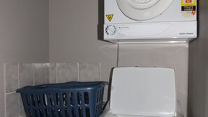 Un lave-linge à chargement frontal, avec un panier à linge bleu posé sur le dessus, un mur blanc et un panneau d’avertissement.