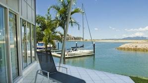 Un espace extérieur ensoleillé comprenant un fauteuil de relaxation, une vue sur une étendue d’eau calme, un quai avec un bateau et une rive rocheuse.