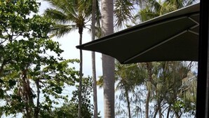A patio with a view of the sea, palm trees, and a fenced area. - Peg's Beach House (Horseshoe Bay)